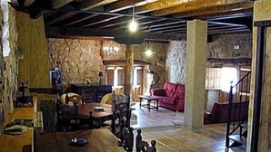 A rustic interior with exposed wooden beams, stone walls, a red sofa, and a stone fireplace.