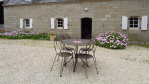A stone building with a gravel courtyard, a table with chairs, and potted plants with pink flowers. - Plobannalec Lesconil: Country holiday home - Plobannalec-Lesconil (Plobannalec-Lesconil)