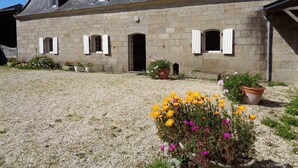 A stone building with a sloped roof, multiple windows with shutters, and a gravel courtyard with potted plants. - Plobannalec Lesconil: Country holiday home - Plobannalec-Lesconil (Plobannalec-Lesconil)