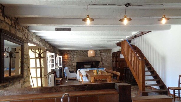A rustic interior with a stone fireplace, wooden staircase, and a dining area with a sink and table. - Plobannalec Lesconil: Country holiday home - Plobannalec-Lesconil (Plobannalec-Lesconil)