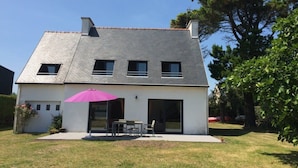 A modern two-story house with a sloped roof, a patio with a table and chairs, and a large tree in the background. - House / Villa - Loctudy (Loctudy)