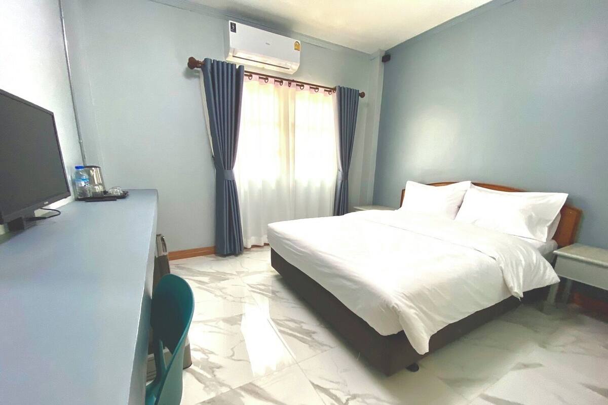 A hotel room with a bed, a desk with a computer, and an air conditioning unit.