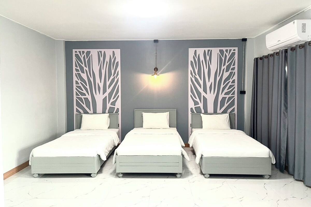 A room with three beds aligned in a row, a ceiling light, and a wall-mounted air conditioner.