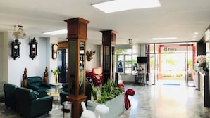A lobby with a green sofa, a white dog statue, a red car model, and a wooden pillar. - Chainatgrand Hotel (Chai Nat)