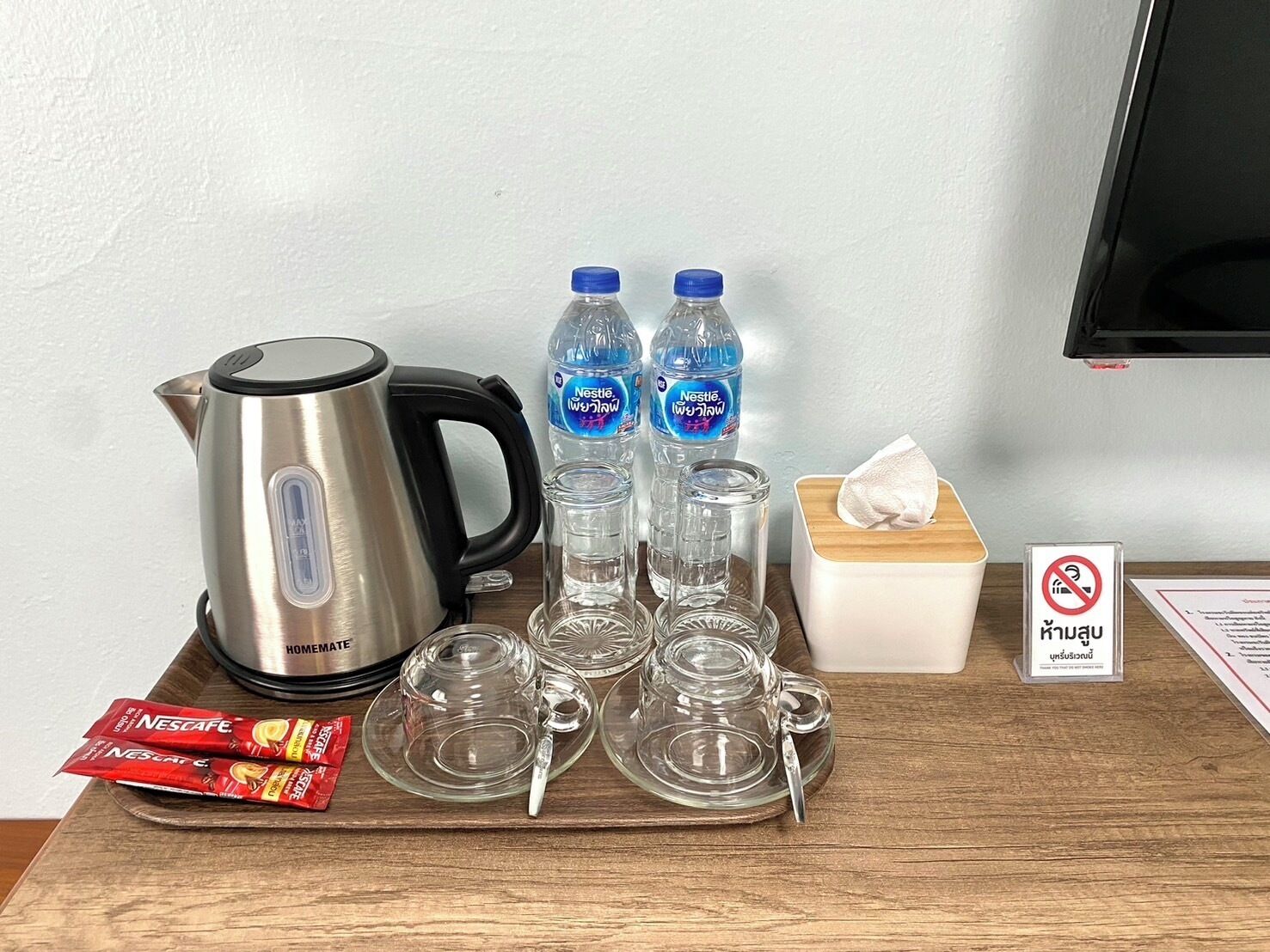A kitchen setup with a kettle, water bottles, a tissue box, and Nescafe packets.