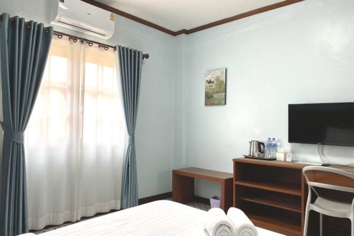 Habitación de hotel con cama, escritorio, silla, televisor y ventana con cortinas.