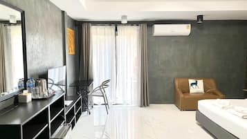 A modern hotel room with a large bed, a desk with a computer, a chair, and a sofa.