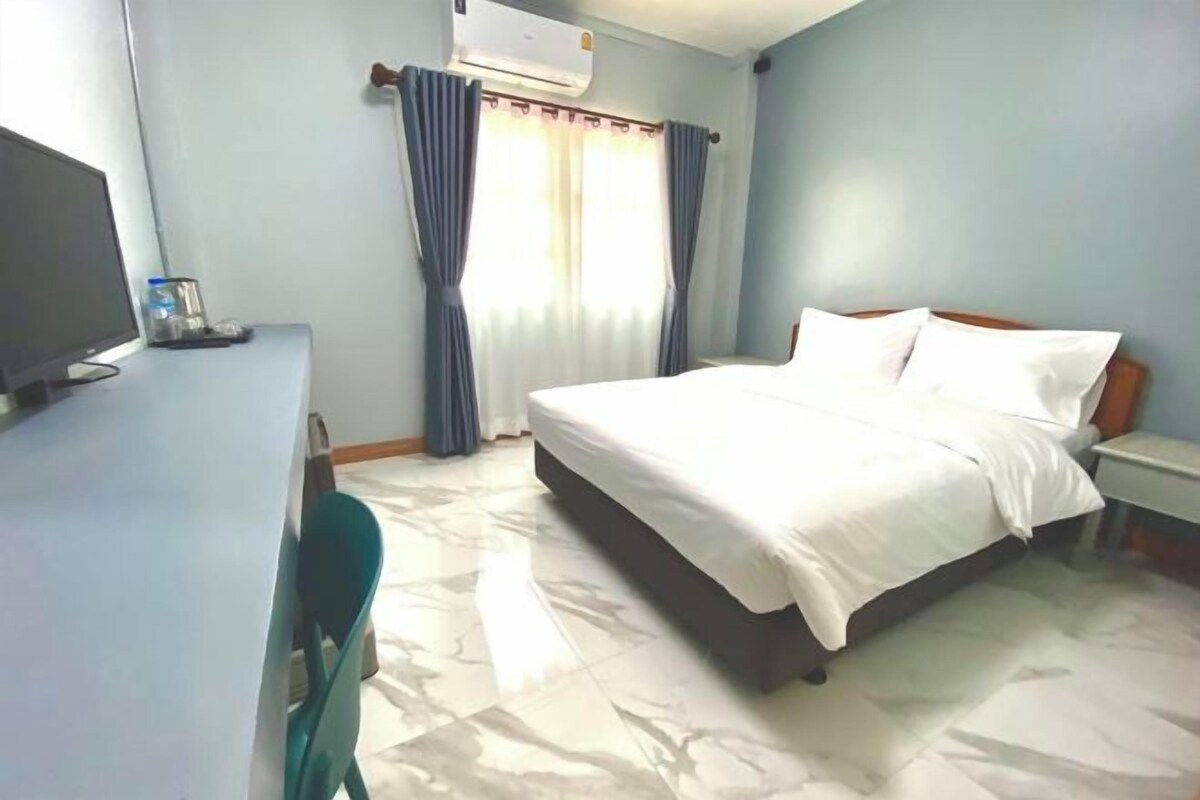 A hotel room with a bed, a desk with a computer, and a window with curtains.