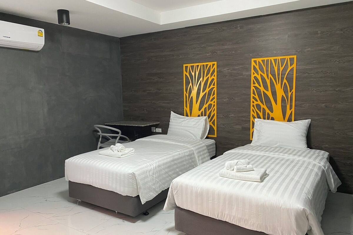 A hotel room with two beds, a small table, a chair, and a wall-mounted air conditioner.