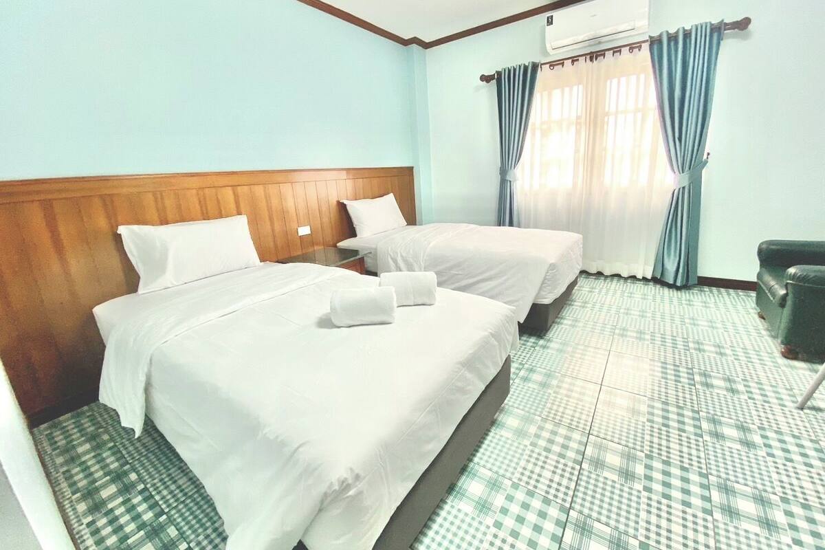 A hotel room with two beds, a wooden headboard, a checkered floor, a desk, and a chair.