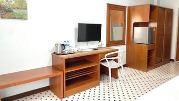 A compact hotel room with a wooden desk, a television, a refrigerator, and a white chair.