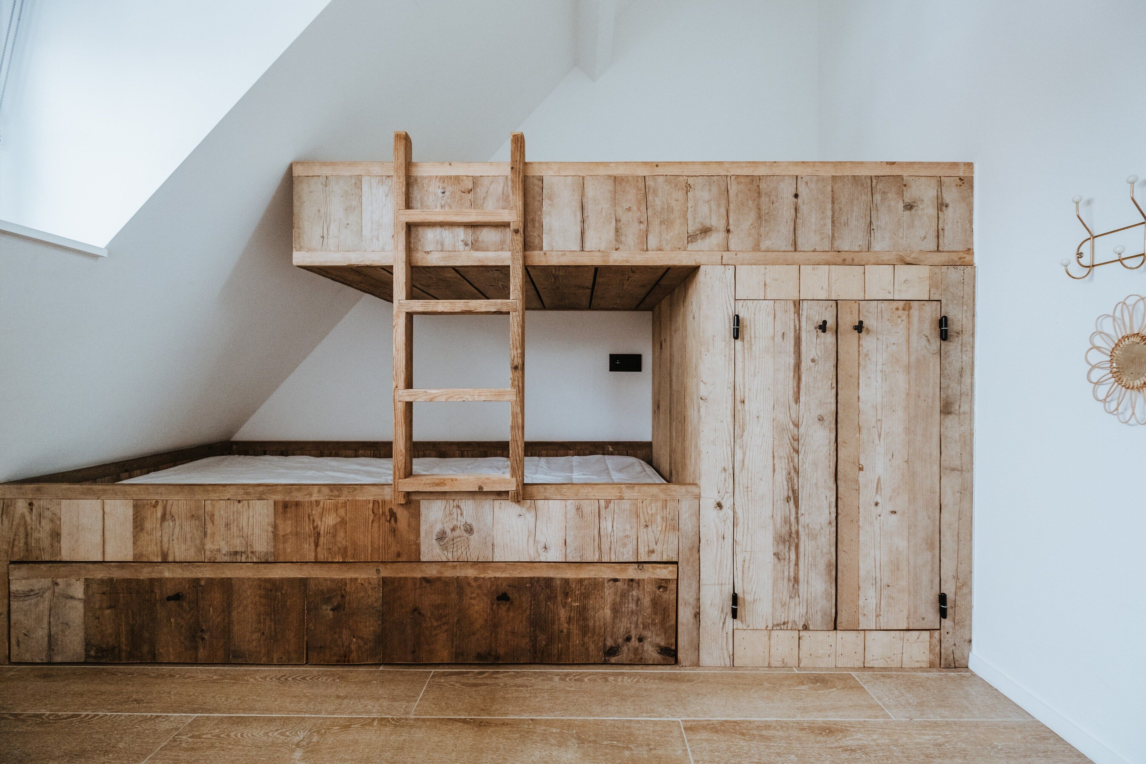 Ein Schlafzimmer im Loft-Stil mit einem hölzernen Etagenbett, einer Stehleiter und einer kleinen, abgeschlossenen Schreibtischgegend.