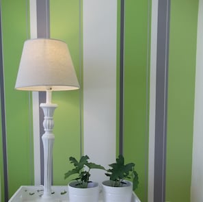 Une table blanche, sur laquelle se trouvent une lampe et deux plantes en pot, est placée devant un mur à rayures vertes.