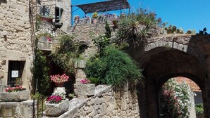 Un bâtiment en pierre doté d’une façade rustique, d’un espace extérieur abrité avec des sièges et d’une rue pavée.