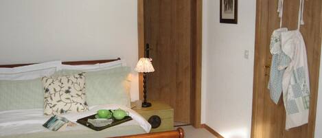 A bedroom with a wooden bed, a nightstand with a lamp, and a door with towels hanging.