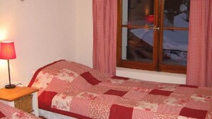 A bedroom with two beds, a wooden headboard, a window with curtains, and a lamp on a bedside table. - Luxury alpine apartment with warm indoor pool, sauna & fitness room (Gstaad)