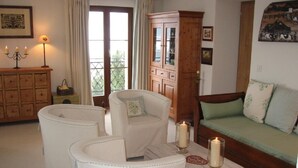 A cozy living room with a green sofa, two white armchairs, a wooden cabinet, and a table with candles. - Luxury alpine apartment with warm indoor pool, sauna & fitness room (Gstaad)