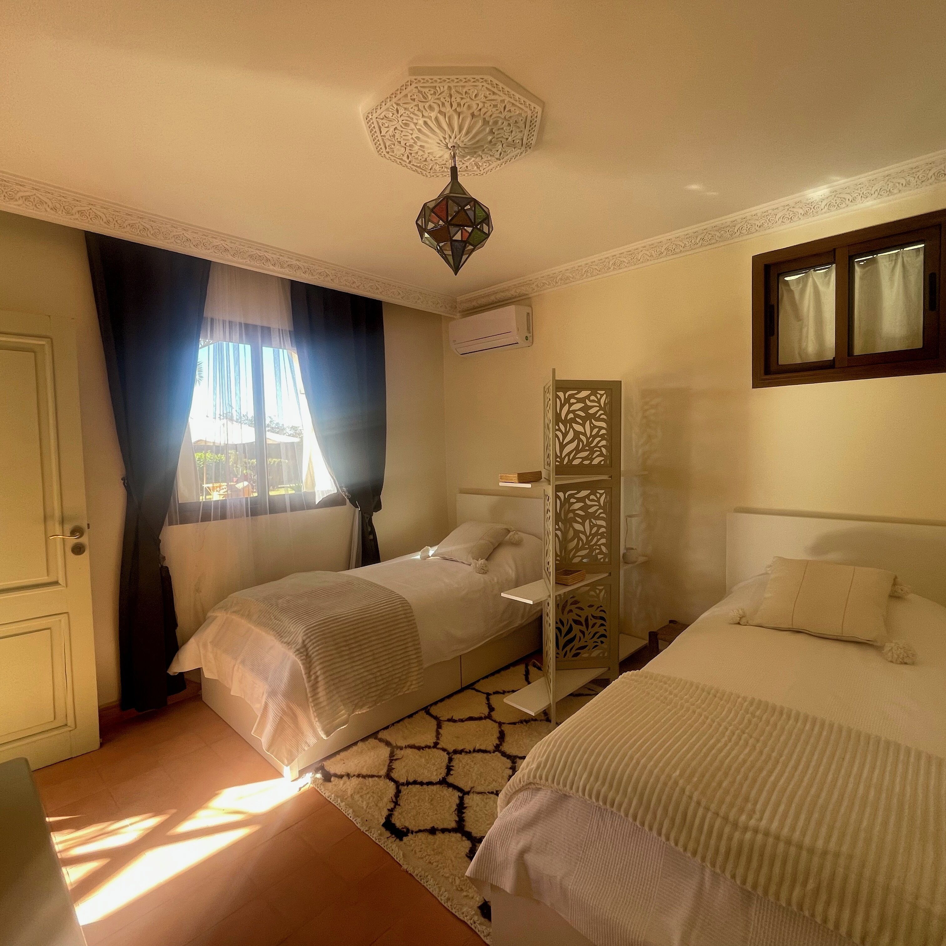 Une chambre avec deux lits, une fenêtre avec des rideaux, un luminaire décoratif au plafond et une étagère intégrée.