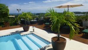 A rooftop pool area with a view of the ocean, surrounded by potted plants and outdoor furniture. - Creole pavilion in the garden. (le francois)