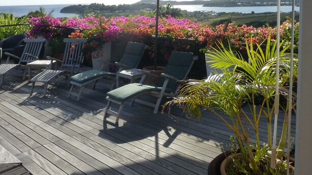 A wooden deck with lounge chairs and a large umbrella, overlooking a scenic view of a lake and hills. - Creole pavilion in the garden. (le francois)