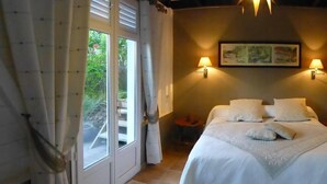 A bedroom with a bed, two wall-mounted lamps, a painting, and a view through a door. - Creole pavilion in the garden. (le francois)