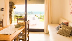 Una habitación con una mesa de madera, cestas de mimbre, un sofá blanco con cojines estampados y vistas al mar a través de una puerta abierta.