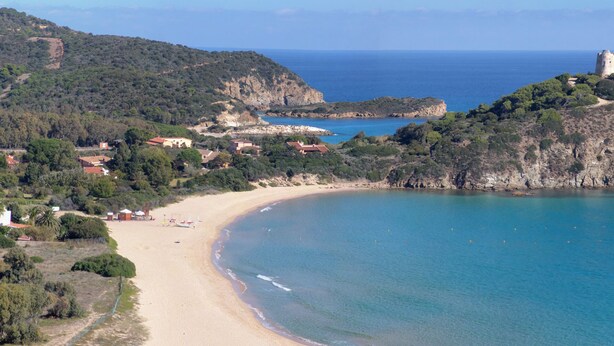 Paisaje costero con una playa, una torre en una colina y edificios dispersos.