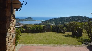 Un muro de piedra con una lámpara colgante, un patio con césped y vistas al mar y las colinas.