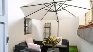 Ein kleiner Außenbereich zum Sitzen mit einem weißen Sonnenschirm, Korbmöbeln und einem Blumenstrauß.