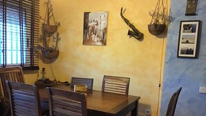 Een eethoek met een houten tafel en stoelen, een hangende plant, een lijst met een afbeelding en een wandlamp.