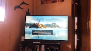 Een woonkamer met een flatscreen televisie aan de muur, een boekenkast met boeken, een geweven salontafel en decoratieve objecten.