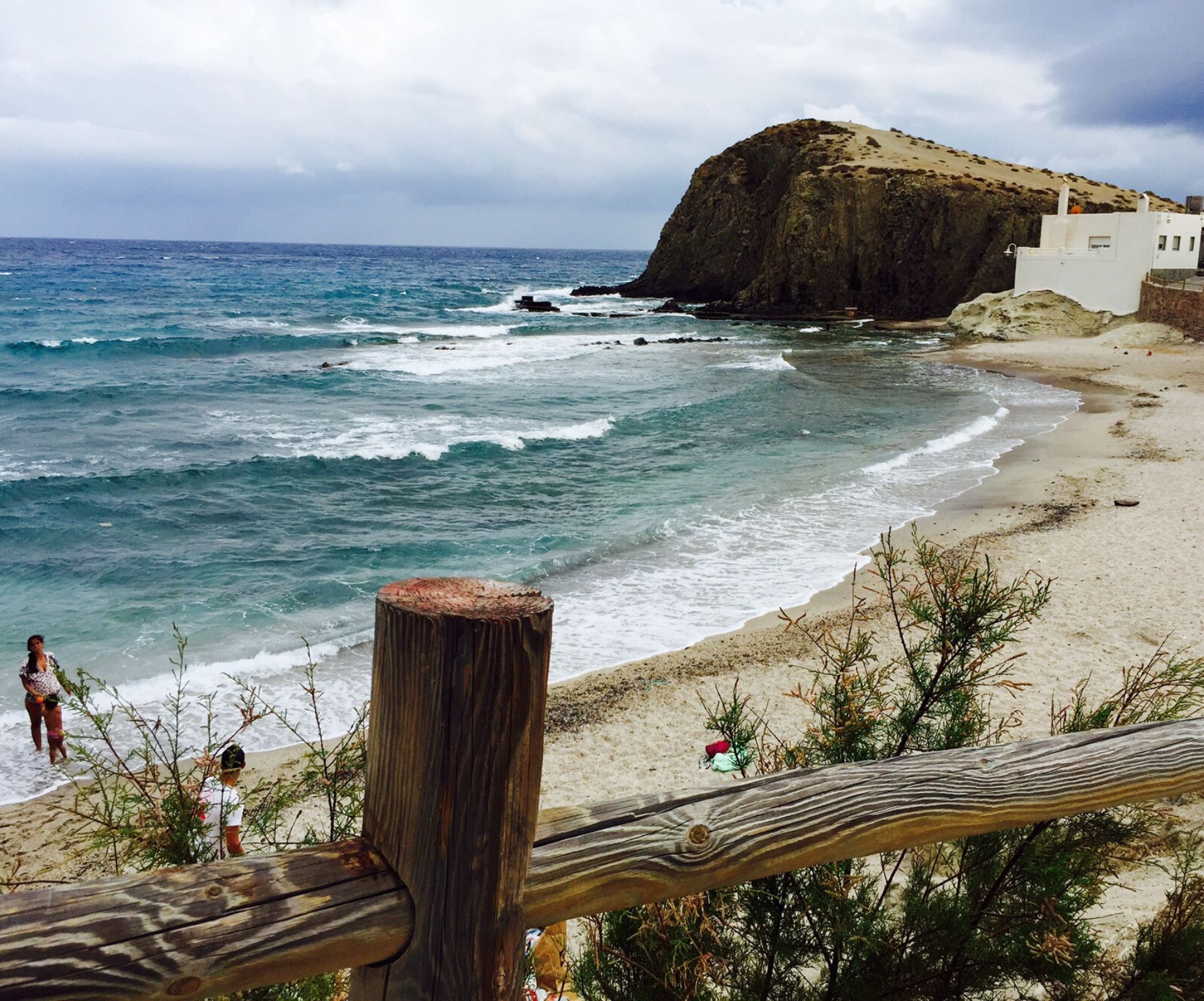A beach with a wooden fence, rocky outcrops, and a building in the background.