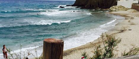 A beach with a wooden fence, rocky outcrops, and a building in the background.