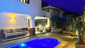 An outdoor swimming pool area with lounge chairs and a sofa, surrounded by a white building with a balcony. - Villa on Mar Menor Golf Resort, Murcia. High quality 3-bed villa with pool. (Torre-Pacheco)