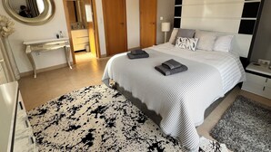 A modern bedroom with a large bed, bedside tables, a mirror, and a ceiling fan. - Villa on Mar Menor Golf Resort, Murcia. High quality 3-bed villa with pool. (Torre-Pacheco)