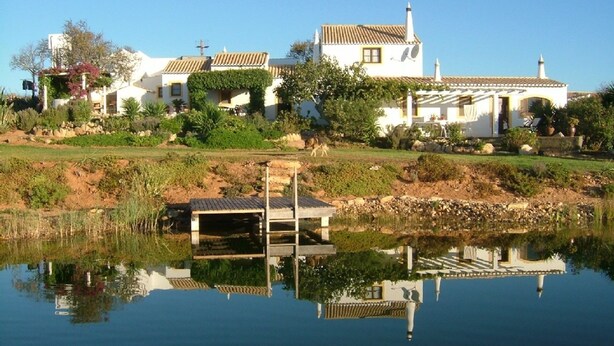 A white villa with a tiled roof, a small dock, and a pond in the foreground. - Villa Celeiro (Atalaia Velha, Lagos)