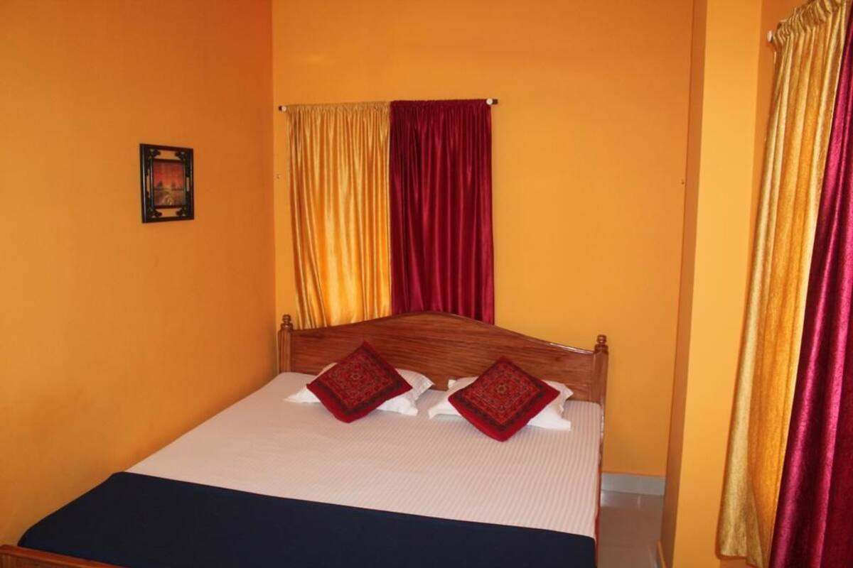 A single bed with a wooden headboard, two red pillows, and a white bedspread.