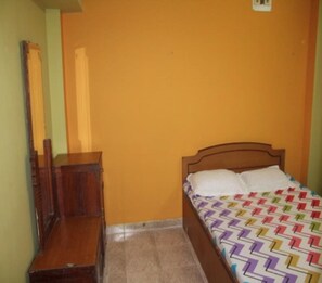 Une chambre avec un lit en bois, une table de chevet et une commode adossées à un mur jaune.