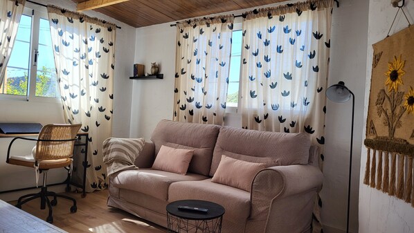 A cozy living room with a beige sofa, a small round table, a wicker chair, and a laptop on a desk. - Sandra's house (Arona)