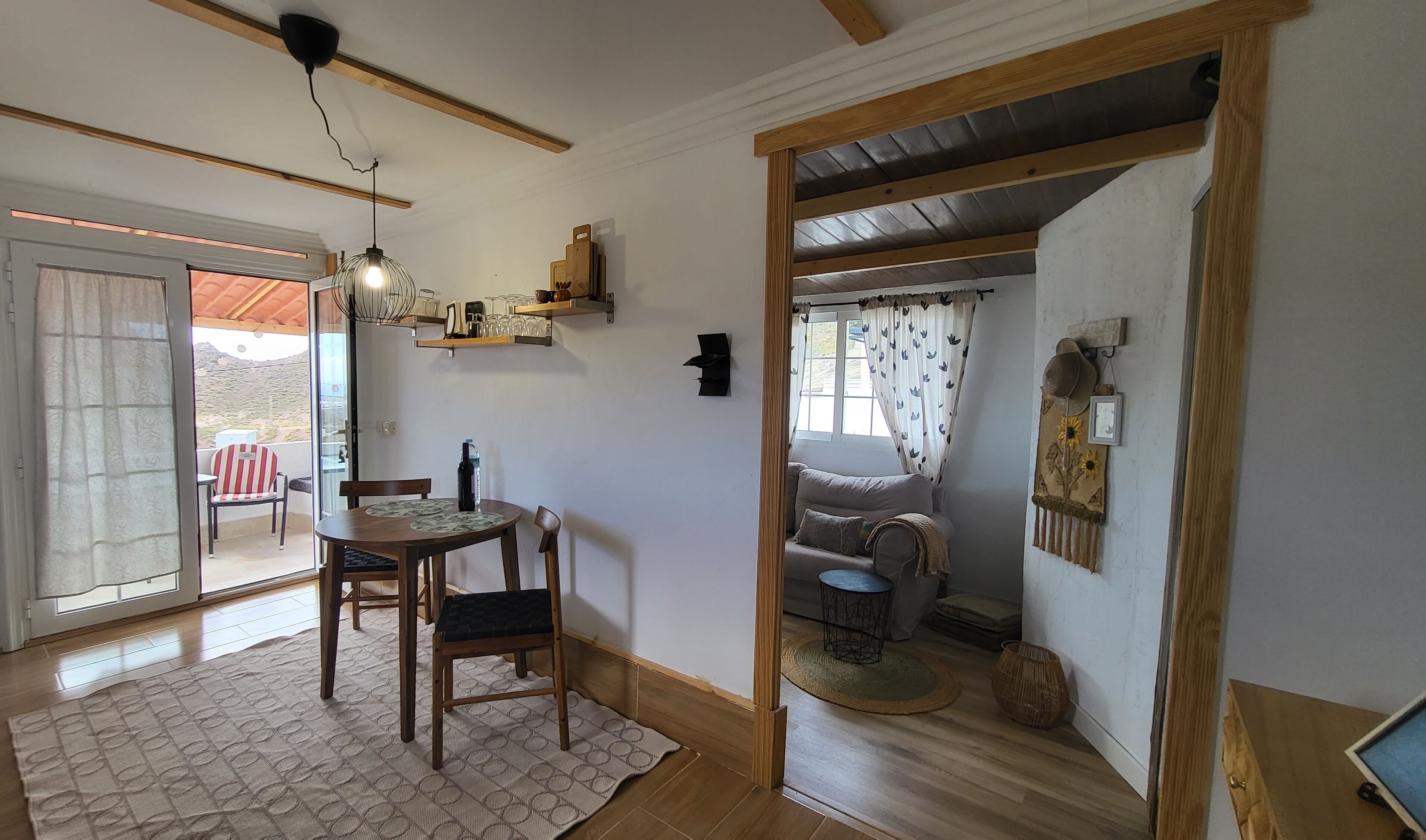 Een eetruimte met een tafel en stoelen, een hanglamp en een uitzicht door een glazen deur op een terras.