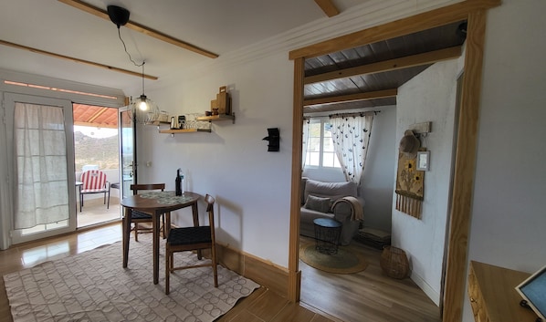 Un coin repas avec une table et des chaises, un luminaire suspendu et une vue sur une terrasse extérieure, accessible par une porte vitrée.