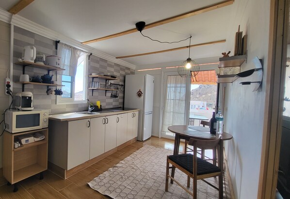 Une cuisine avec des meubles blancs, un four à micro-ondes, un réfrigérateur et un coin repas comprenant une table et des chaises.