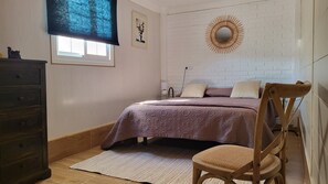 A bedroom with a bed, a wooden dresser, a chair, a small table with a lamp, and a wall-mounted mirror. - Sandra's house  (Arona)
