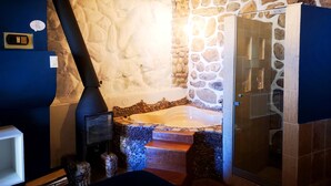 A bathroom with a stone wall, a bathtub, and a shower area. - Cities of the World - Apartments Cusco (Cusco)