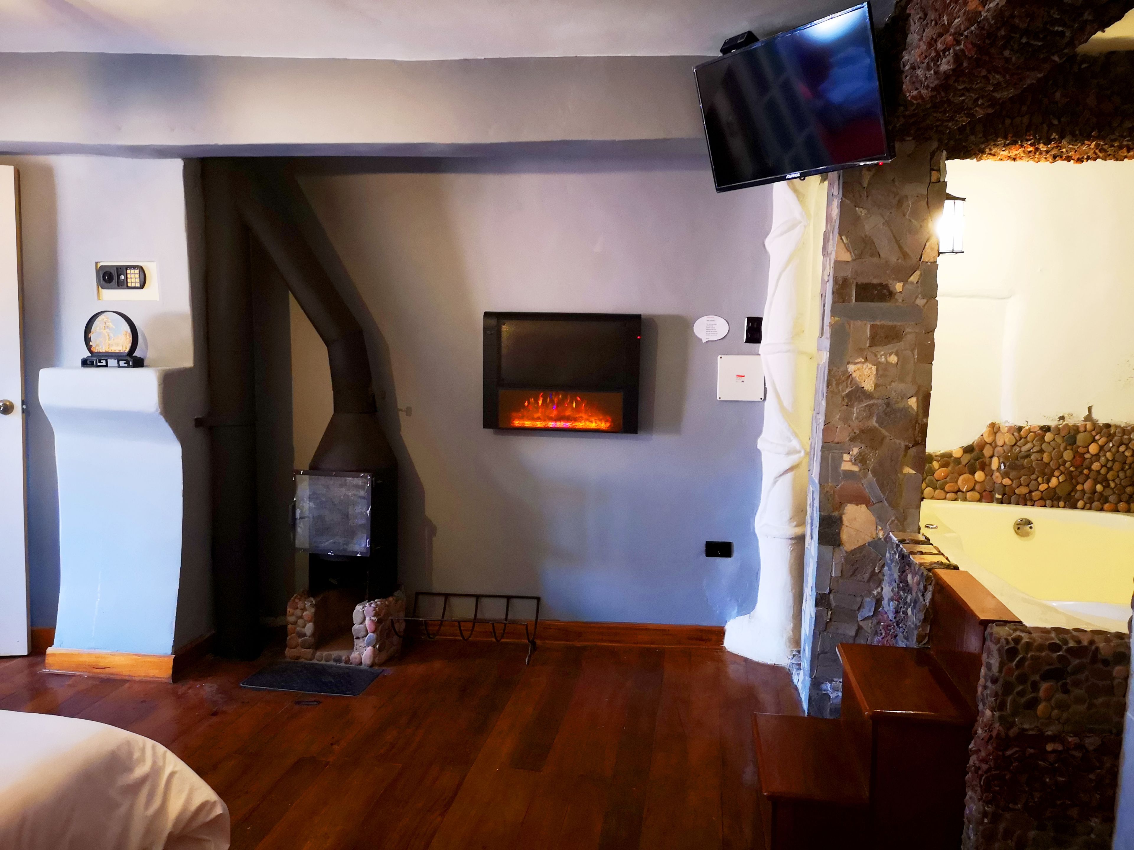 A room with a stone fireplace, a mounted television, and a stone wall.