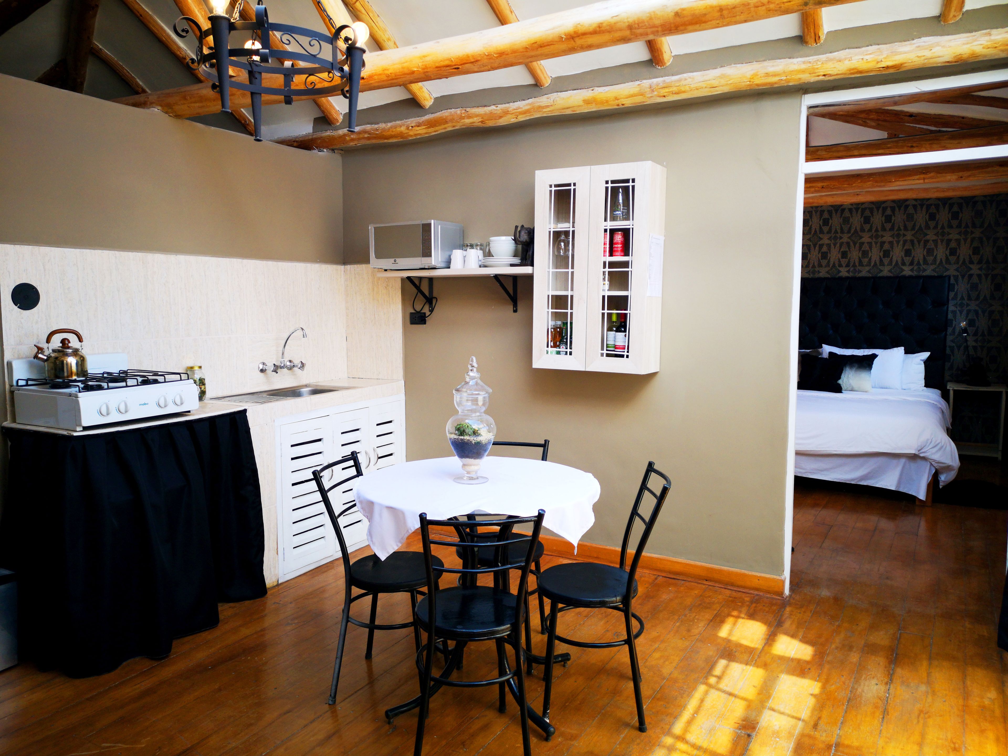 A compact kitchen with a gas stove, a microwave, and a sink. There is a dining area with a table and chairs. The room has wooden flooring and a sloped ceiling with exposed beams.