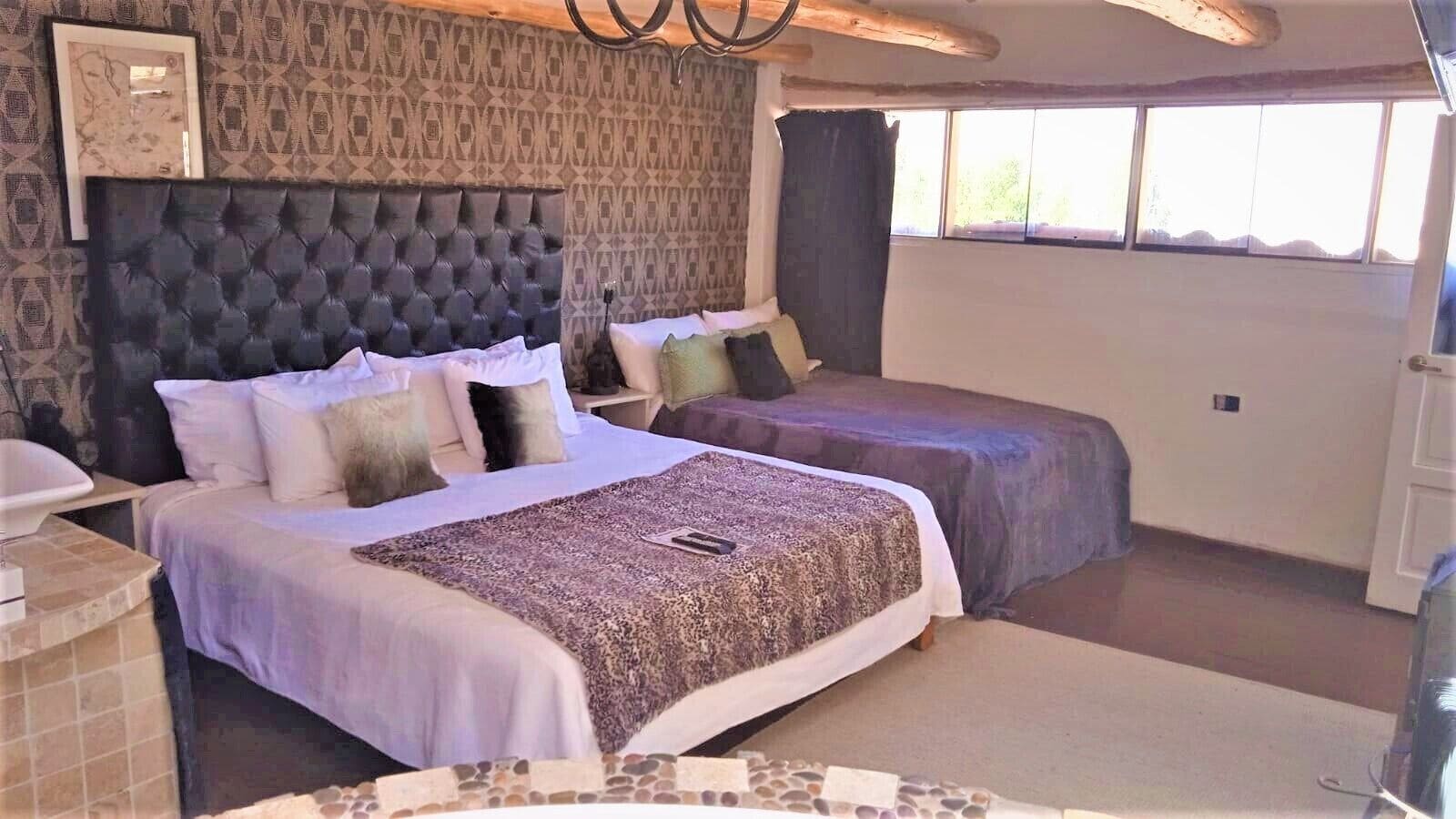 A hotel room with two beds, a patterned headboard, a window with curtains, and a tiled floor.