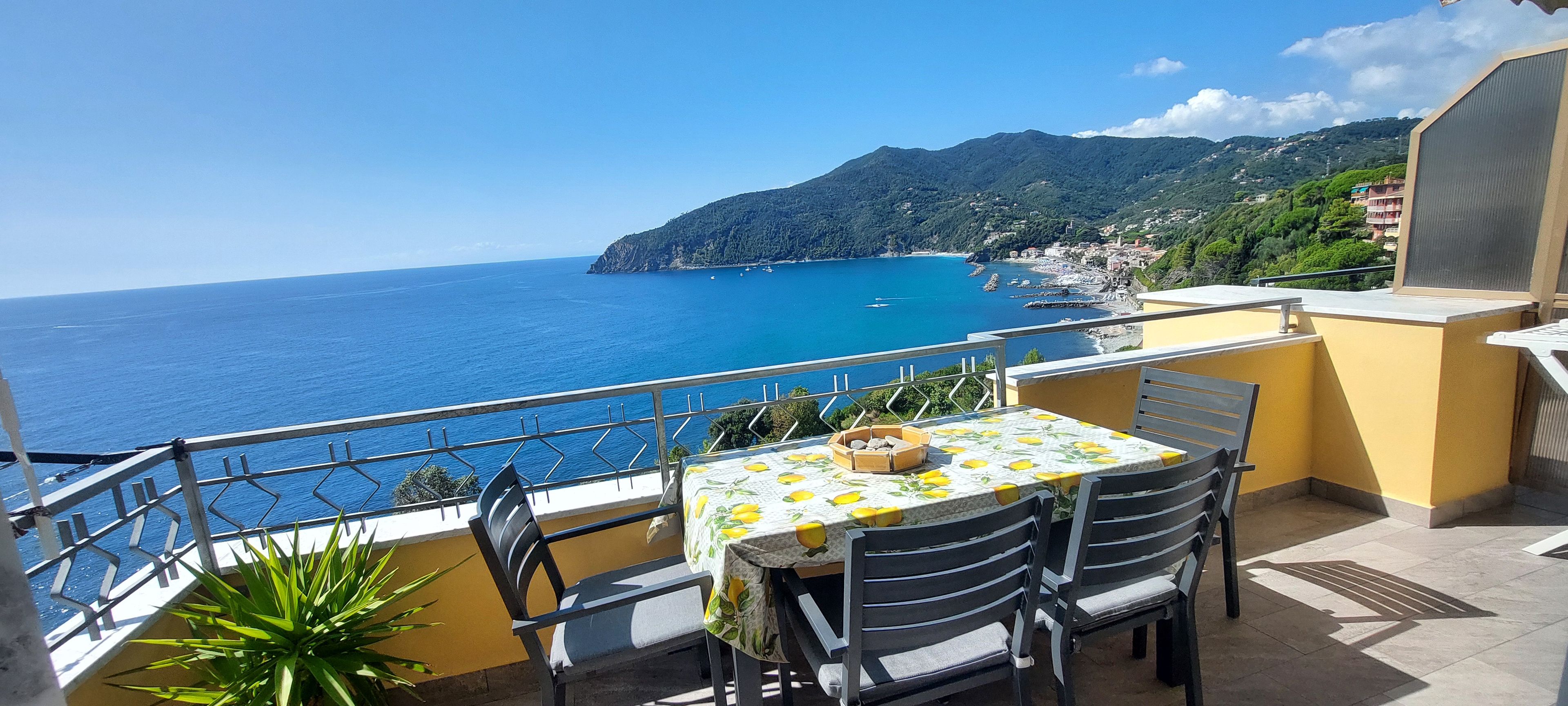 A terrace with a table and chairs overlooking a coastal view.