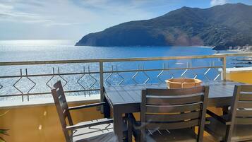 Un balcon avec une table et des chaises donnant sur une vue côtière, avec une montagne en arrière-plan.