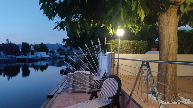 Ein ruhiger Sitzbereich im Freien mit einer Bank, einem Stuhl, einer Lampe und Blick auf ein stilles Gewässer und sanfte Hügel.